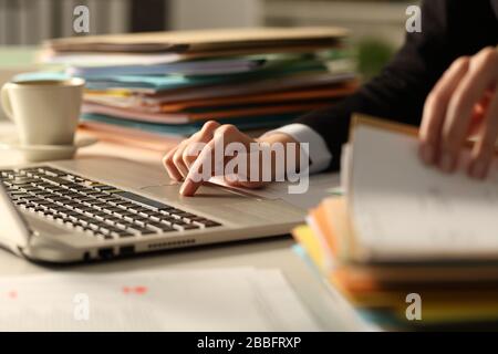 Nahaufnahme von Führungskräften, die in der Nacht mit einem Laptop im Büro hart arbeiten, um einen Stapel von Dokumenten zu überprüfen Stockfoto