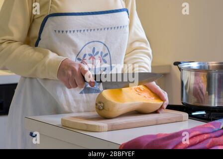 Frau in der Küche mit vier Kochfeldern zum Schneiden von Butternusskürbis zur Herstellung von Suppe Stockfoto