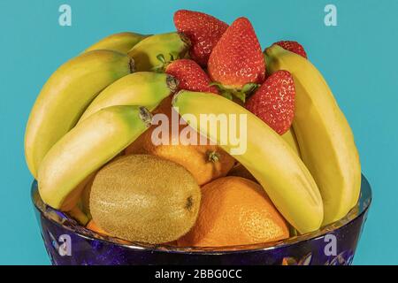 Frische tropische und subtropische Früchte in einer großen blauen Kristallvase. Isolierter, blauer Hintergrund. Stockfoto