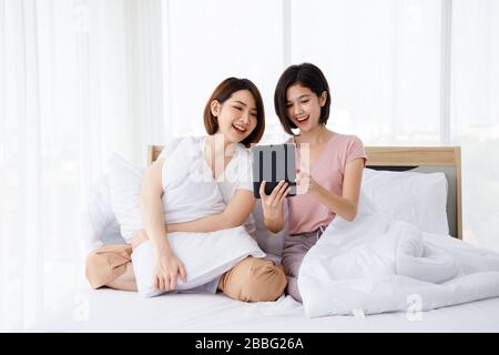 Zwei glückliche Asiaten legen sich auf das Bett und benutzen Tablette. Konzept für Aktivitäten im Teenageralter oder im Freundeskreis, Lifestyle zu Hause und romantische Momente. Stockfoto