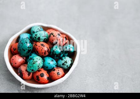 Bemalte rote und blaue Wachteleier für Ostern in kleiner Keramikplatte auf grauem Betongrund. Leere Stelle für Text und Zeichen. Stockfoto