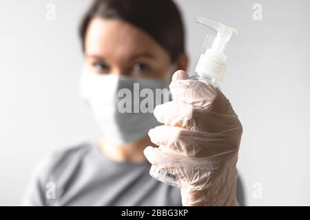 Coronavirus Konzept. Mädchen, die eine schützende medizinische Maske tragen, die eine Flasche mit Desinfektionsmittel hält. Hand Sie einen sterilen medizinischen Handschuh ein. Hygiene während einer Pandemie Stockfoto