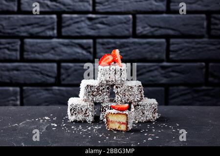 Traditionelle Lamingtons Vanilleschwamm Minikuchen mit Erdbeermarmeladenschicht innen, mit Schokolade überzogen und auf einem T mit geraspelter Kokosnuss bestrichen Stockfoto