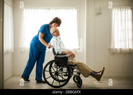 Lachender älterer Mann, der von einer weiblichen Krankenschwester in den Rollstuhl gedrückt wird. Stockfoto