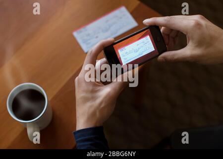 Hände eines jungen Mannes, der einen Scheck mit einem Smartphone fotografiert. Stockfoto