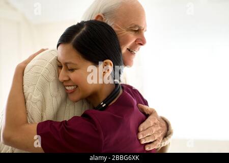 Lächelnd weibliche Krankenschwester umarmt einen älteren männlichen Patienten. Stockfoto