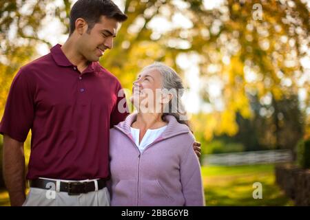 Lächelnde ältere Frau und ein Pfleger ein Gespräch, während Sie durch einen Park gehen. Stockfoto