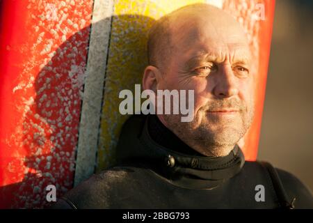 Inhalt mittelerwachsener Mann steht mit seinem Surfbrett im Sonnenschein. Stockfoto