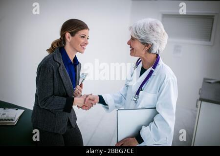 Lächelnde Ärztin schüttelt mit einem Pharmavertreter in einem Krankenhaus die Hände. Stockfoto