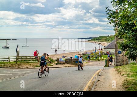 Radfahrer, die an einem geschäftigen Sommertag am Strand am niedrigen Newton-By-the-Sea vorbeifahren. Northumberland, Großbritannien. August 2018. Stockfoto