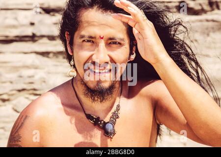 Outdoor-Porträt von modischem Langhaarjungen Mann mit Bindi und Schmuck Stockfoto