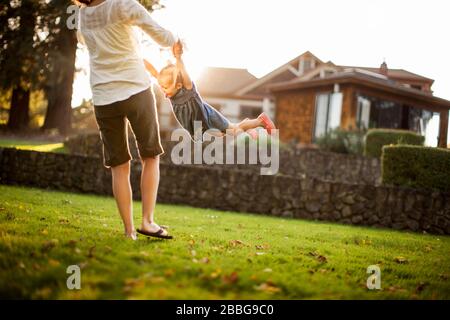 Mitte der erwachsenen Frau spielerisch Spinnen ihre glücklichen jungen Tochter um im Hinterhof Stockfoto