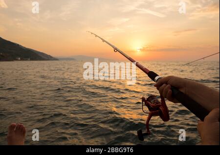 Es gibt ein Paar und sie angeln, während die Sonne untergeht. Sie sitzen auf einem Gerüst und einer von ihnen hält Angelrute gegen Sonnenuntergang. Stockfoto