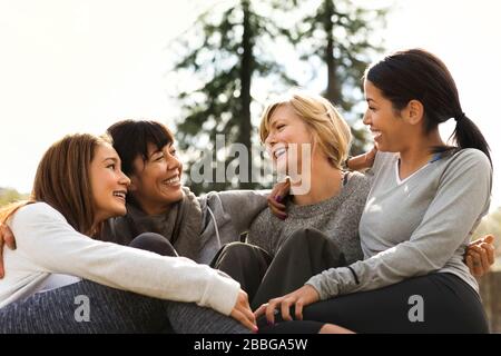 Vier junge Frauen sitzen zusammen und haben Spaß in einem Park Stockfoto