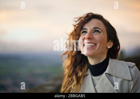 Porträt einer fröhlichen jungen Frau, die lächelt, während sie den Himmel betrachtet Stockfoto