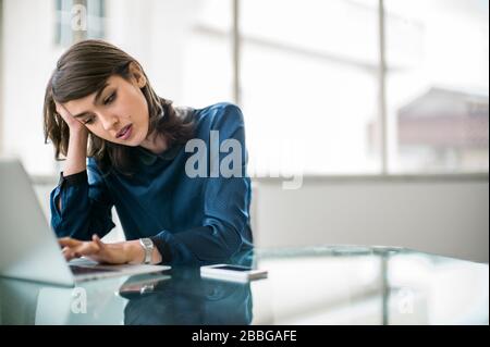 Unglückliche junge Geschäftsfrau kämpfen, um die Arbeit auf ihrem Laptop-Computer zu beenden Stockfoto