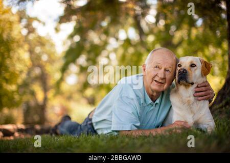 Glücklicher älterer Mann liegt mit seinem Hund in einem sonnigen Garten Stockfoto