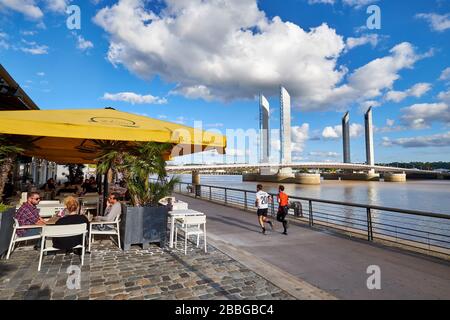 Blick auf die vertikale Brücke Jacques Chaban-Delmas am Garonne-Fluss mit Café-Terrasse und zwei männlichen auf dem Laufsteg am Flussufer Stockfoto