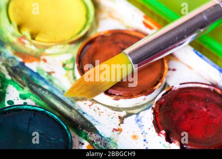 Nahaufnahme eines gebrauchten Farbpaintkastens, Lacke und Pinsels in Farbe Stockfoto