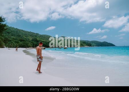 Cote D'Or Beach, Praslin Seychelles Tropical Island, junge Männer schwimmen kurz am weißen Strand mit riesigen Felsbrocken und Felsen und einem weißen tropischen Stockfoto