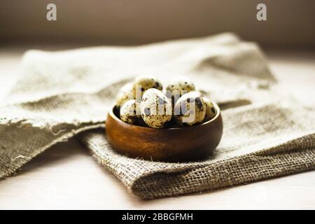 Wachteleier in runder Bambusschale auf Sack Leinwand auf Holzhintergrund. Gesunde Ernährung, Osterkonzept. Stockfoto