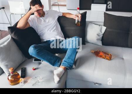 Der junge Mann gucken in seiner eigenen Wohnung fernsehen. Alkoholisches Sitzen auf dem Sofa, das geöffnete Flaschen mit Whisky amoooooing. Leiden Sie unter Kopfschmerzen oder Hängeschmerzen. Allein mit Stockfoto