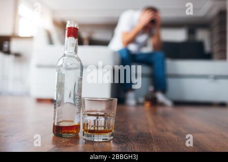 Der junge Mann gucken in seiner eigenen Wohnung fernsehen. Bild mit verschwommenem Hintergrund, bei dem der Mann auf der Couch sitzt und Kopfschmerzen hat. Alkoholiker hat Stockfoto