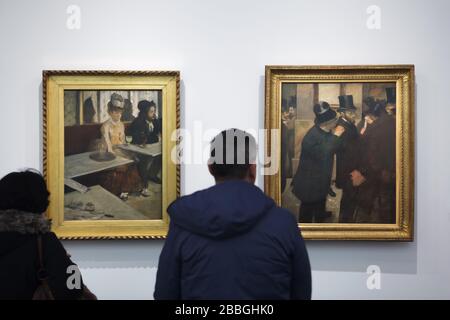 Besucher vor den Gemälden des französischen impressionistischen Künstlers Edgar Degas im Musée d'Orsay in Paris, Frankreich. Gemälde "Absinthe drinker" ('Glas Absinthe') aus den Jahren 1875-1876 und "Porträts an der Börse" aus den Jahren 1878-1879 sind von links nach rechts abgebildet. Stockfoto