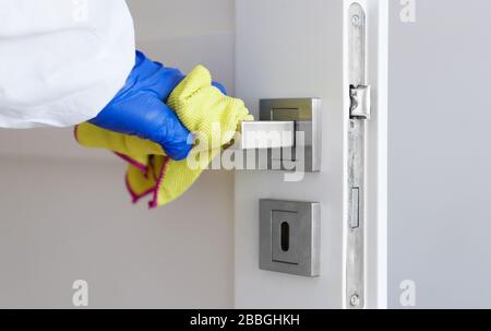 Hand in Schutzhandschuh mit Lappen, der den Türgriff reinigen kann. Covid-19 Desinfektionskonzept. Stockfoto