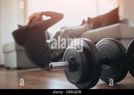 Der junge normale Mann geht zu Hause für Sport ein. Schnitteblick auf einen Anfänger oder Neuling bei Trainingsaktivitäten in seiner Wohnung. Hanteln auf Bildern liegen auf Stockfoto