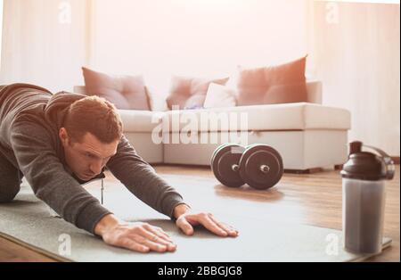 Der junge normale Mann geht zu Hause für Sport ein. Schnitteansicht des Anfängers, der seinen Körper streckt und die Hände auf die Matte foward zieht. Verbesserung der Körperform. Echter Mann Stockfoto