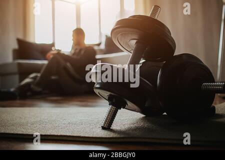 Der junge normale Mann geht zu Hause für Sport ein. Dunkle Sicht auf den müden männlichen Vorson nach dem Training auf dem Boden sitzen und ruhen. Gewöhnlicher Kerl nach dem Training. Dunkel Stockfoto