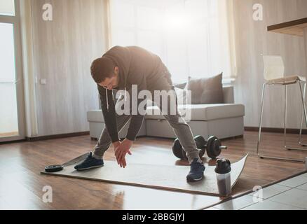 Der junge normale Mann geht zu Hause für Sport ein. Erwachsene männliche Person, die sich mit den Händen bis zu den Füßen streckt. Erwärmen Sie den Körper vor dem ersten Training. Freshman und Stockfoto