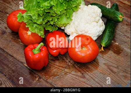 Frisches Gemüse mit Tropfen Wasserpfeffer, Blumenkohl, Salat, Gurken, Tomate auf dem Hintergrund eines alten Holztisches. Stockfoto