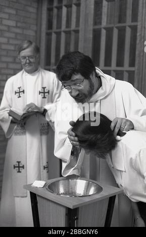 1970er Jahre, historisch, in einer Kirche, eine Frau, die getauft wird, während ein gekleideter Priester ihren Kopf bettet, South London, England, Großbritannien. Die Taufe ist ein christlicher Einlassritus, ein Sakrament, eine Verordnung Jesu Christi. Stockfoto