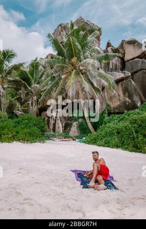 Cote D'Or Beach, Praslin Seychelles Tropical Island, junge Männer schwimmen kurz am weißen Strand mit riesigen Felsbrocken und Felsen und einem weißen tropischen Stockfoto