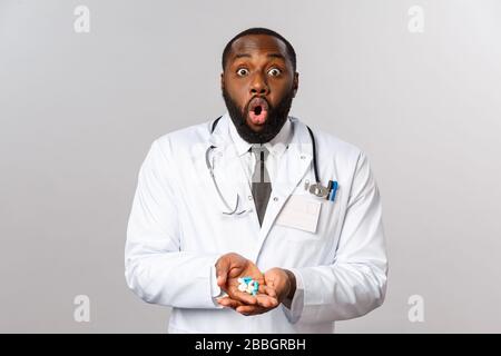 Konzept für Grippe, Krankheit, Gesundheitswesen und Medizin. Staunender afroamerikanischer bärtiger Arzt im weißen Mantel, vergasend gewundert, sieht Kamera beeindruckt aus Stockfoto