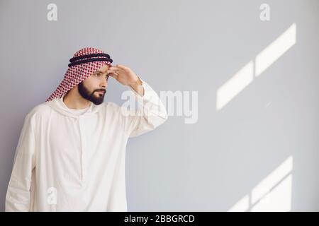 Attraktiver lächelnder arabischer Mann, der auf einem grauen Hintergrund nach Text blickt. Stockfoto