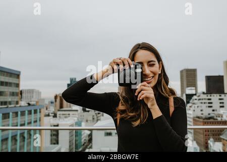 Frau, die auf der Terrasse steht, fotografiert mit einer Sofortkamera. Weibliche Klickbilder mit polaroid-kamera. Stockfoto