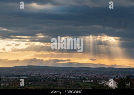 Dramatische Sonnenstrahlen durch niedrige Wolken über der Stadt bei Sonnenuntergang. Die Sonne durchschneidet die Wolken über der Stadt. Sonnenstrahlen auf der Stadt Stockfoto