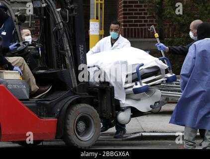 New York, USA. März 2020. Ein in weißem Stoff gewickelter Körper wird von einem Kühlwagen zu einem Gabelstapler entladen und von medizinischen Mitarbeitern, die Schutzmasken, Ausrüstung und Kleidungsstücke tragen, als Schutz vor COVID-19-Kontamination im Brooklyn Hospital Center in New York City am Dienstag, den 31. März 2020, gehandhabt. New Yorks Fälle haben 75.000 und 1.550 Menschen starben. Foto von John Angelillo/UPI Credit: UPI/Alamy Live News Stockfoto