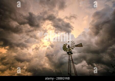 Sonnenuntergang mit Stürmen, die an der Decke vorbeirollen, und einer ländlichen Windmühle im Vordergrund in Kansas United States Stockfoto