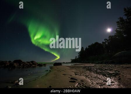 Aurora tanzt über Wasser unter einem Vollmond im Lake Winnipeg, Manitoba Canada Stockfoto