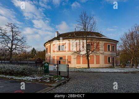 Prag/Tschechien - 31. März 2020: Haupteingang der Festung Chodov mit eisernem Zaun. Park mit Bäumen und Gras, das mit Schnee bedeckt ist. Sonniger Morgen. Stockfoto