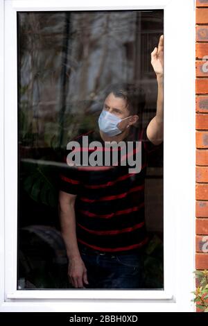 Portrait des männlichen mittleren 40-er, von Fenster ins Haus betrachtet, während Coronavirus abstürzt. Stockfoto