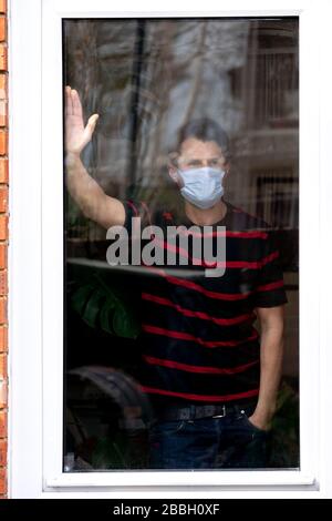 Portrait des männlichen mittleren 40-er, von Fenster ins Haus betrachtet, während Coronavirus abstürzt. Stockfoto