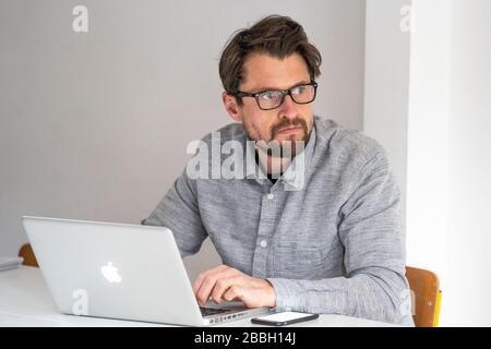 MID 40er-Mann, der von zu Hause aus mit einem Apple-Laptop arbeitet. Stockfoto