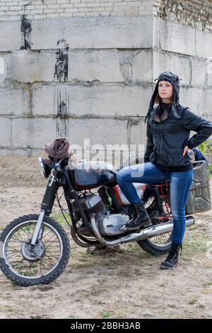 Eine postapokalyptische Frau in der Nähe des Motorrads in der Nähe eines zerstörten Gebäudes Stockfoto