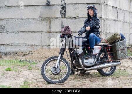 Eine postapokalyptische Frau auf dem Motorrad in der Nähe des zerstörten Gebäudes Stockfoto