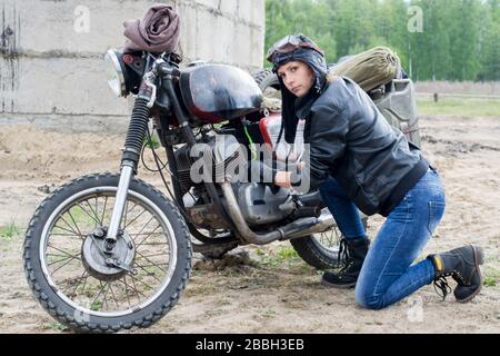Eine postapokalyptische Frau in der Nähe des Motorrads in der Nähe eines zerstörten Gebäudes Stockfoto